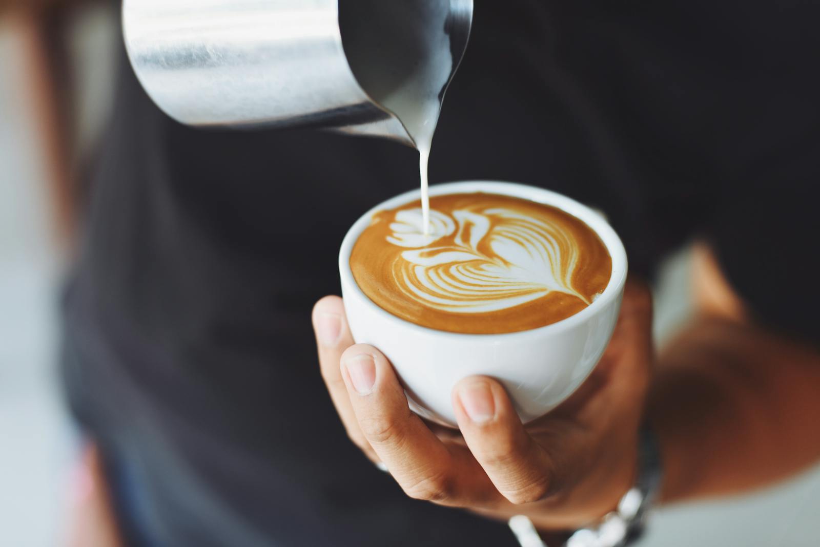 Coffee Calorie Calculation - Close-up of a barista pouring milk to create latte art in a coffee cup.